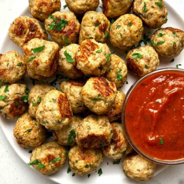 close up of chicken meatballs on plate; side of tomato sauce in bowl.