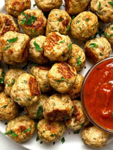 close up of chicken meatballs on plate; side of tomato sauce in bowl.