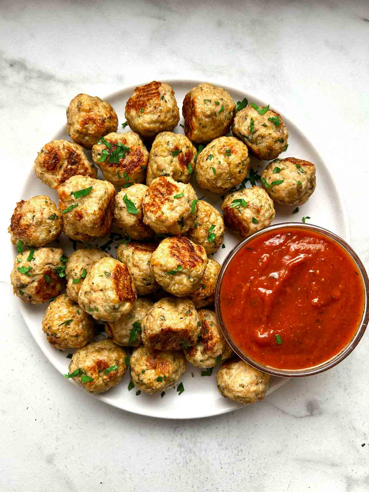 close up of chicken meatballs on plate; side of tomato sauce in bowl.