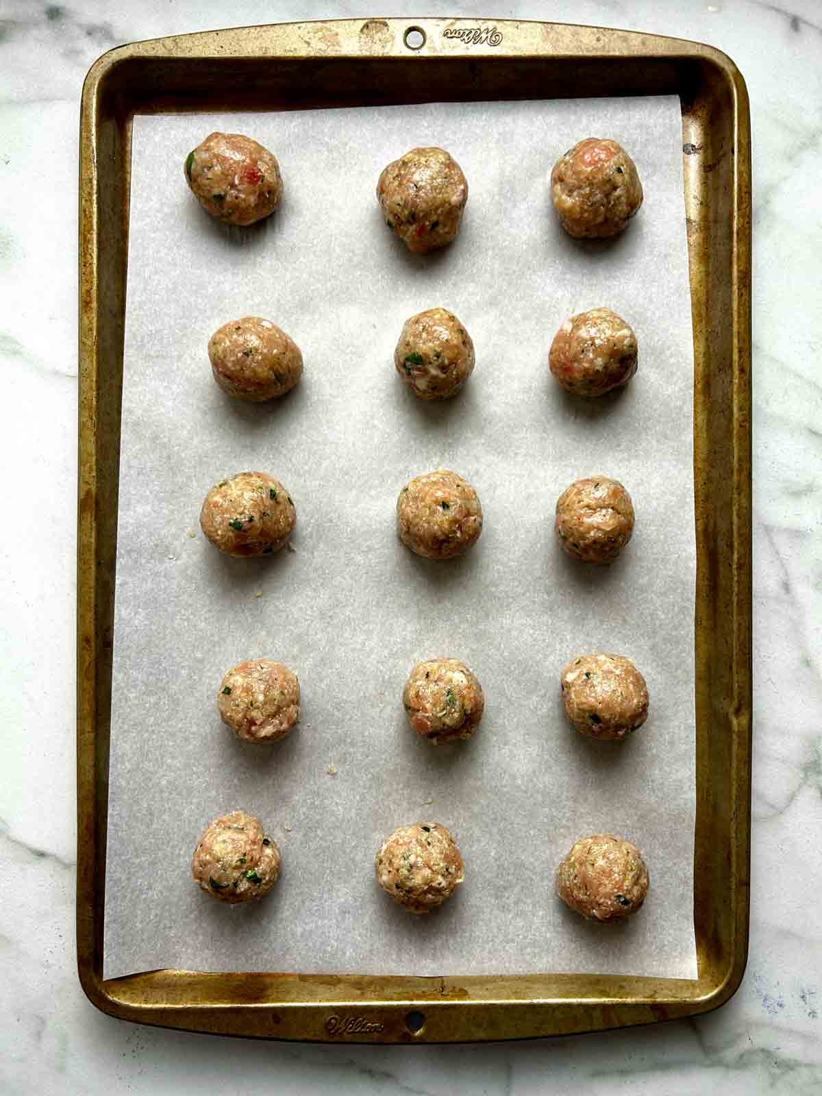 meatball mixture shaped into balls and arranged on parchment-lined baking sheet.