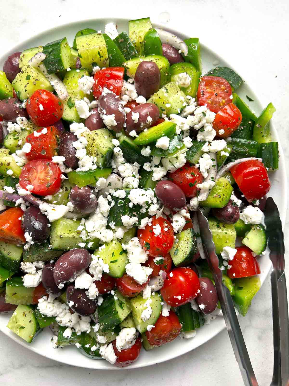 Greek salad on plate with tongs.