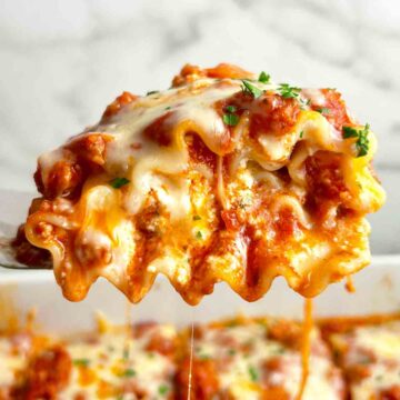 spatula lifting up lasagna roll up; sauce and cheese oozing out.