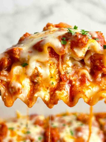 spatula lifting up lasagna roll up; sauce and cheese oozing out.