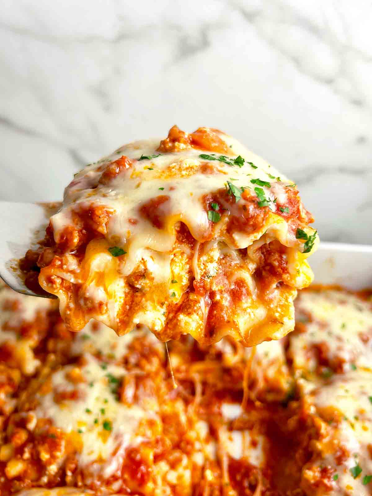 spatula lifting up lasagna roll up; sauce and cheese oozing out.