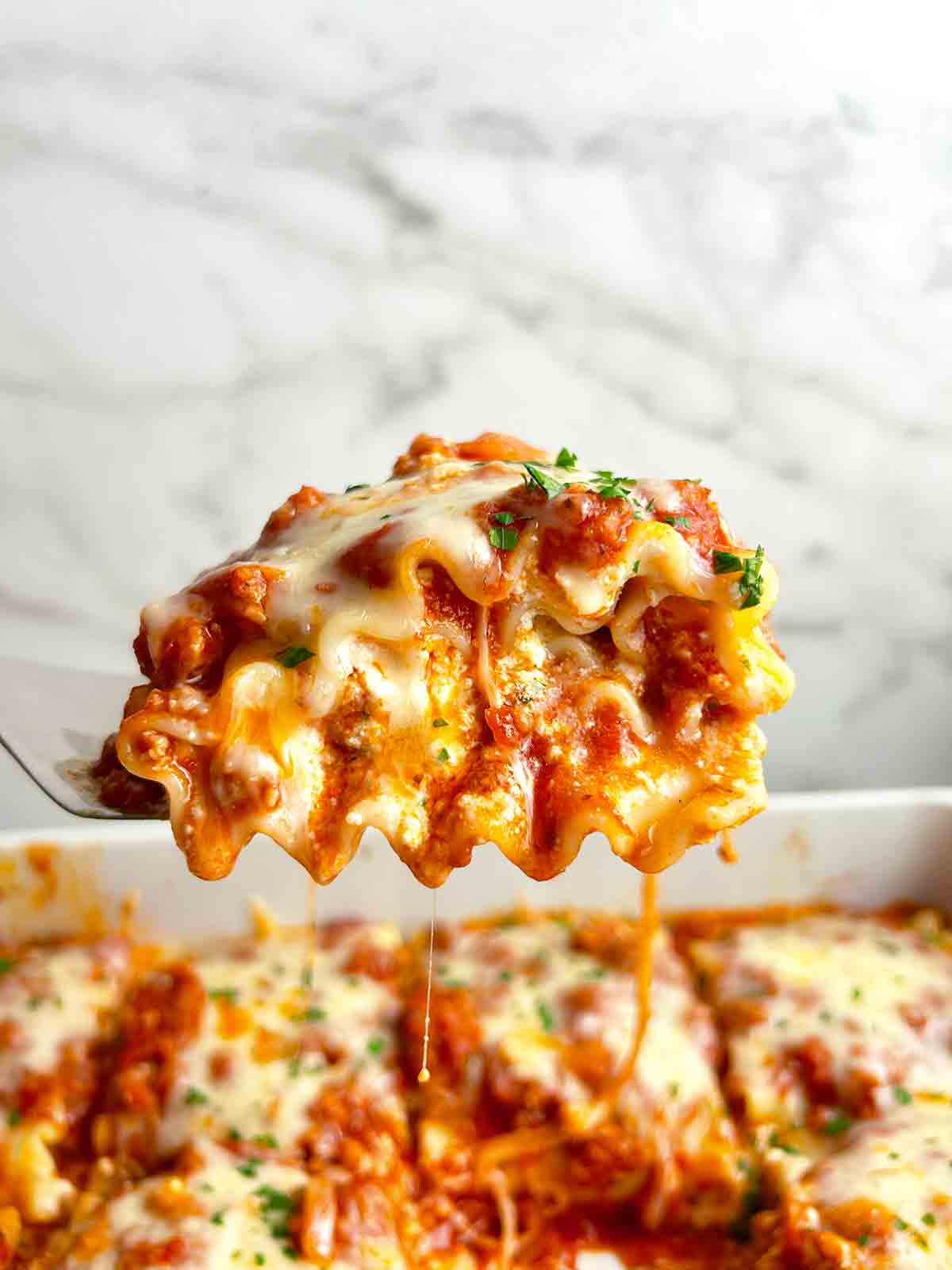 spatula lifting up lasagna roll up; sauce and cheese oozing out.