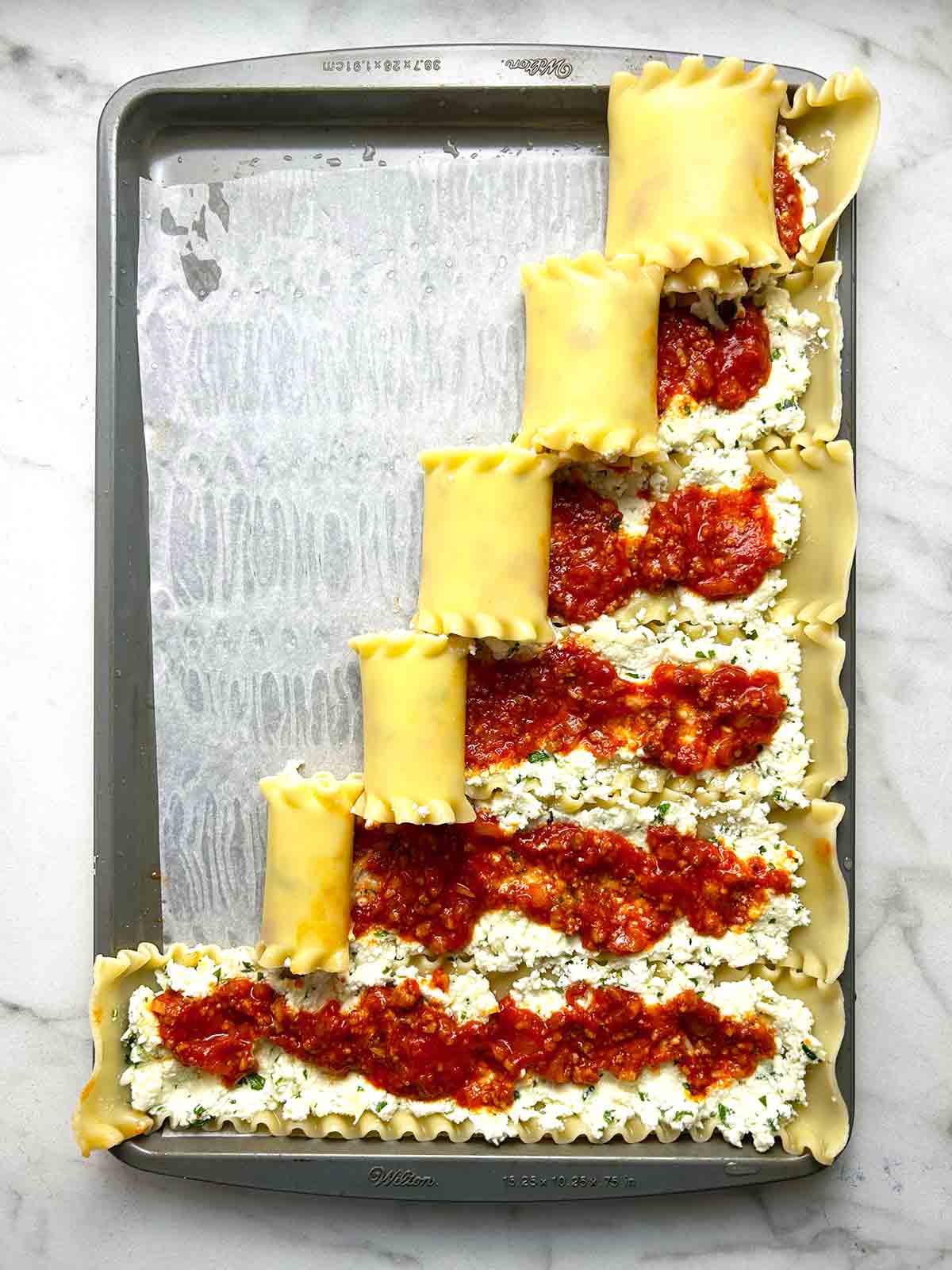 lasagna rolls being rolled on baking sheet.