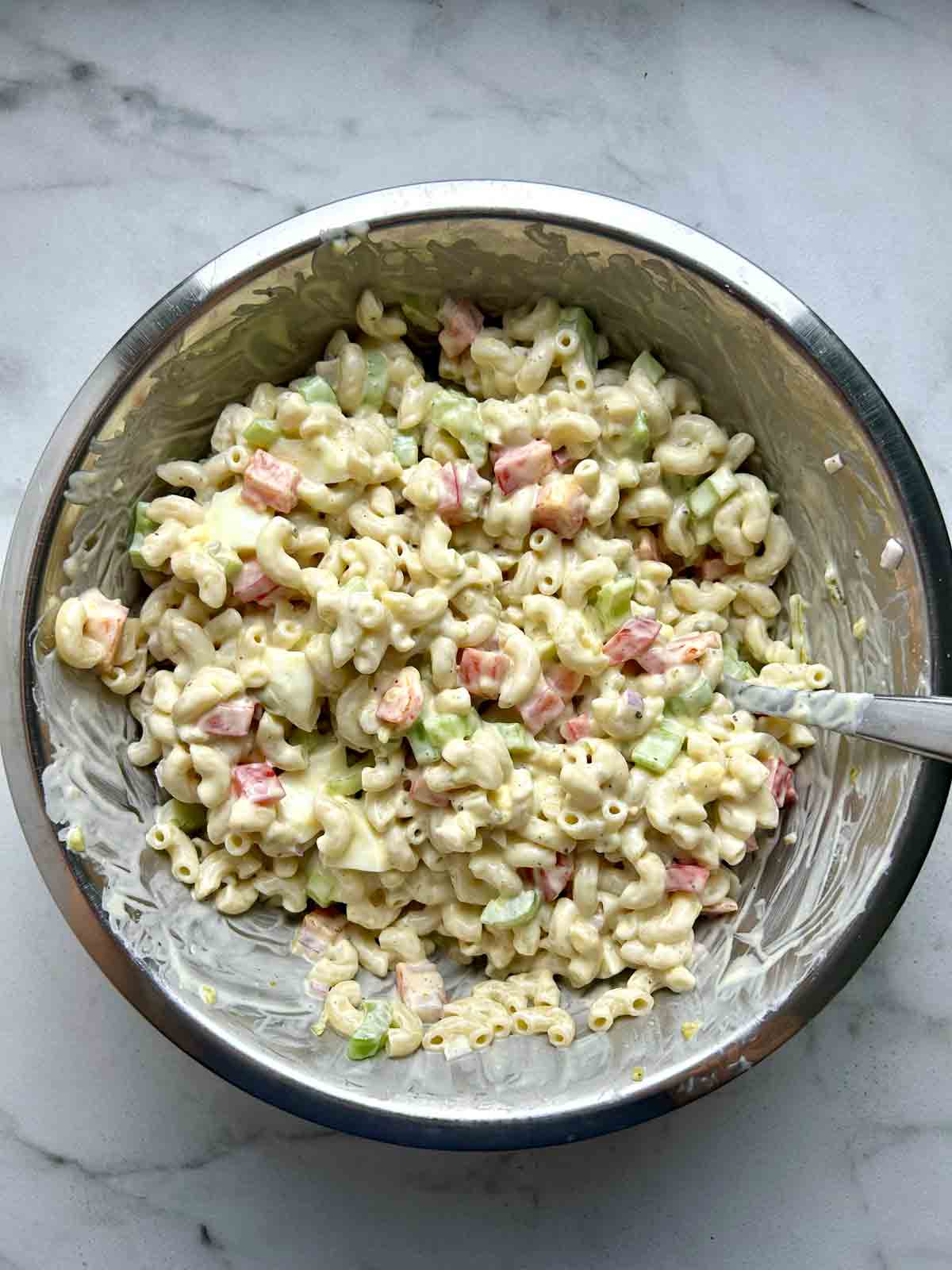 dressing mixed with macaroni and vegetables in metal bowl.