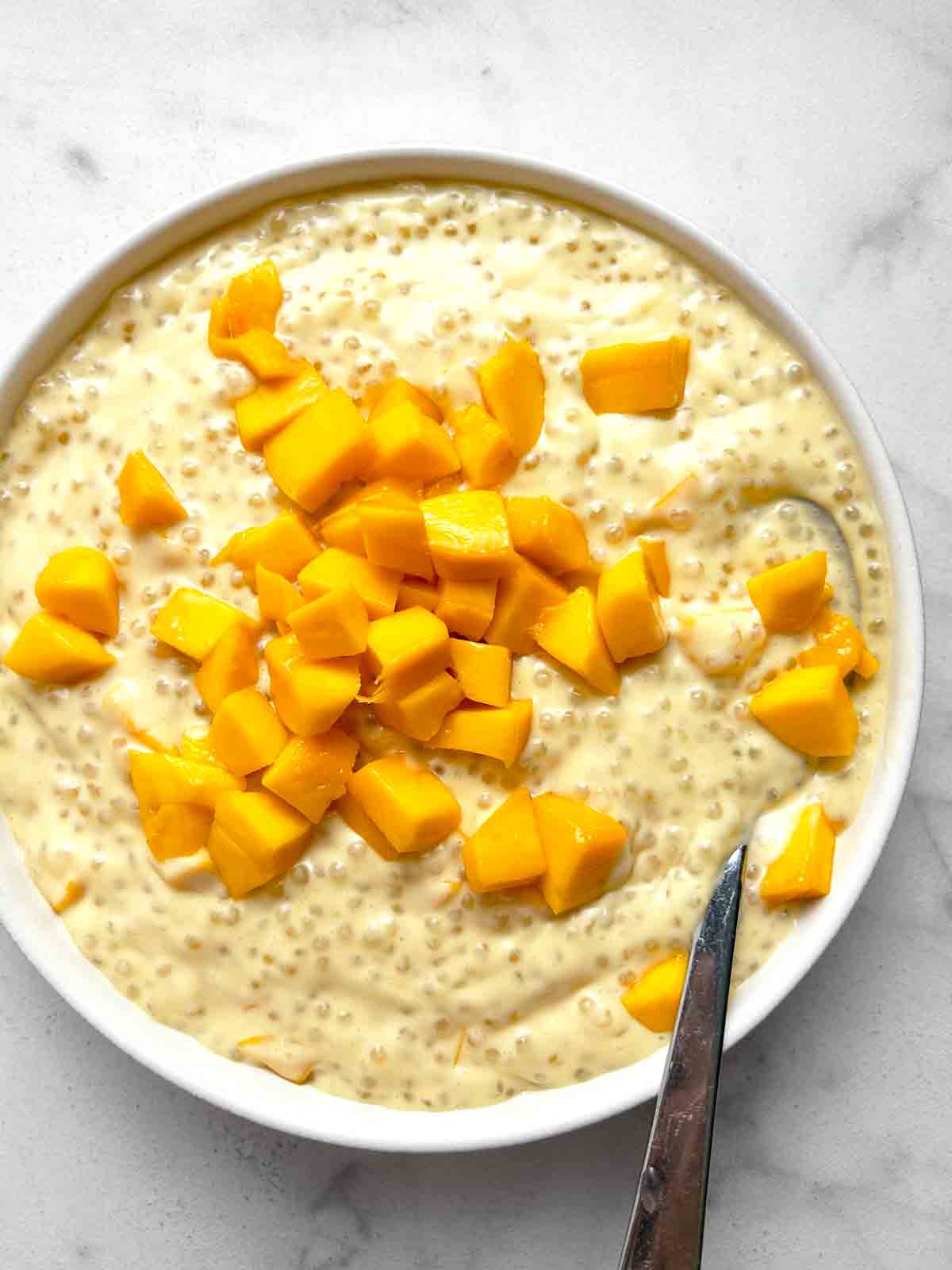 close up of mango sago in bowl with spoon in it.