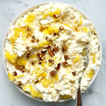 bowl of pina colada fluff with spoon in it; extra walnuts garnished on top.