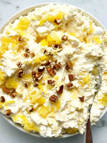 bowl of pina colada fluff with spoon in it; extra walnuts garnished on top.