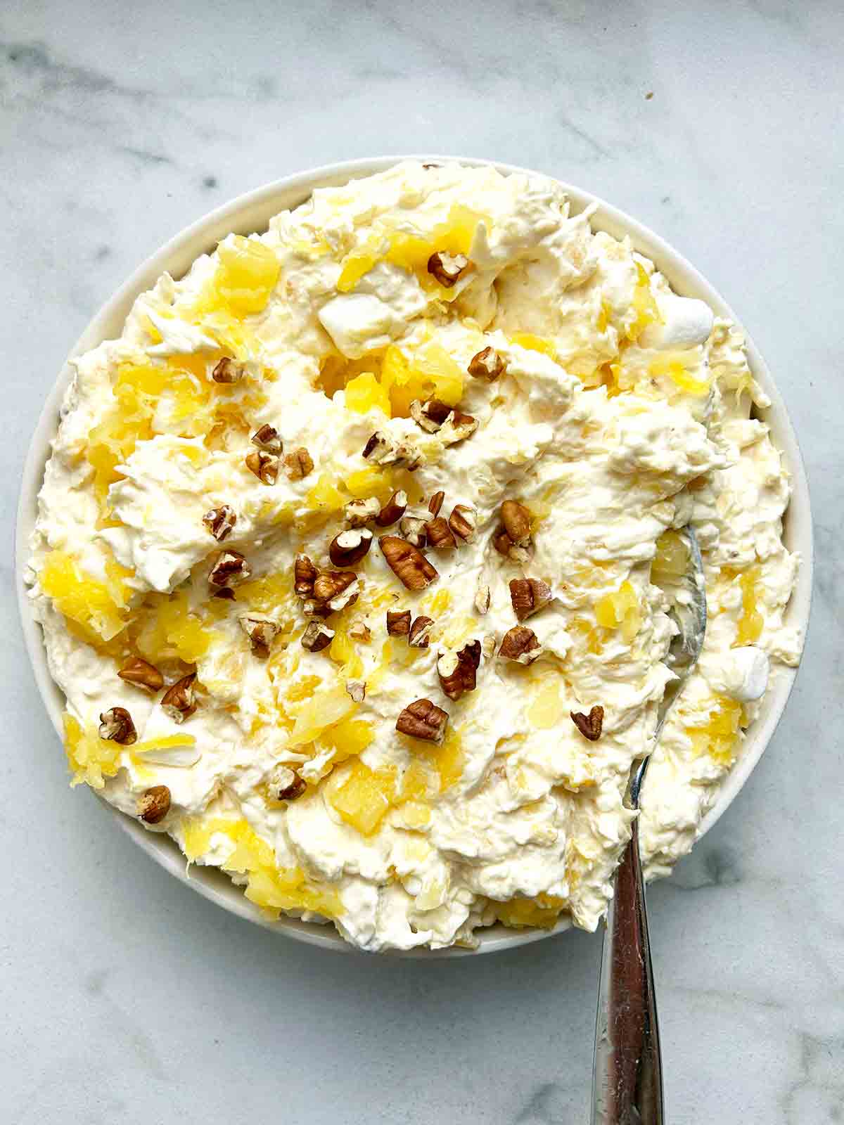 bowl of pina colada fluff with spoon in it; extra walnuts garnished on top.