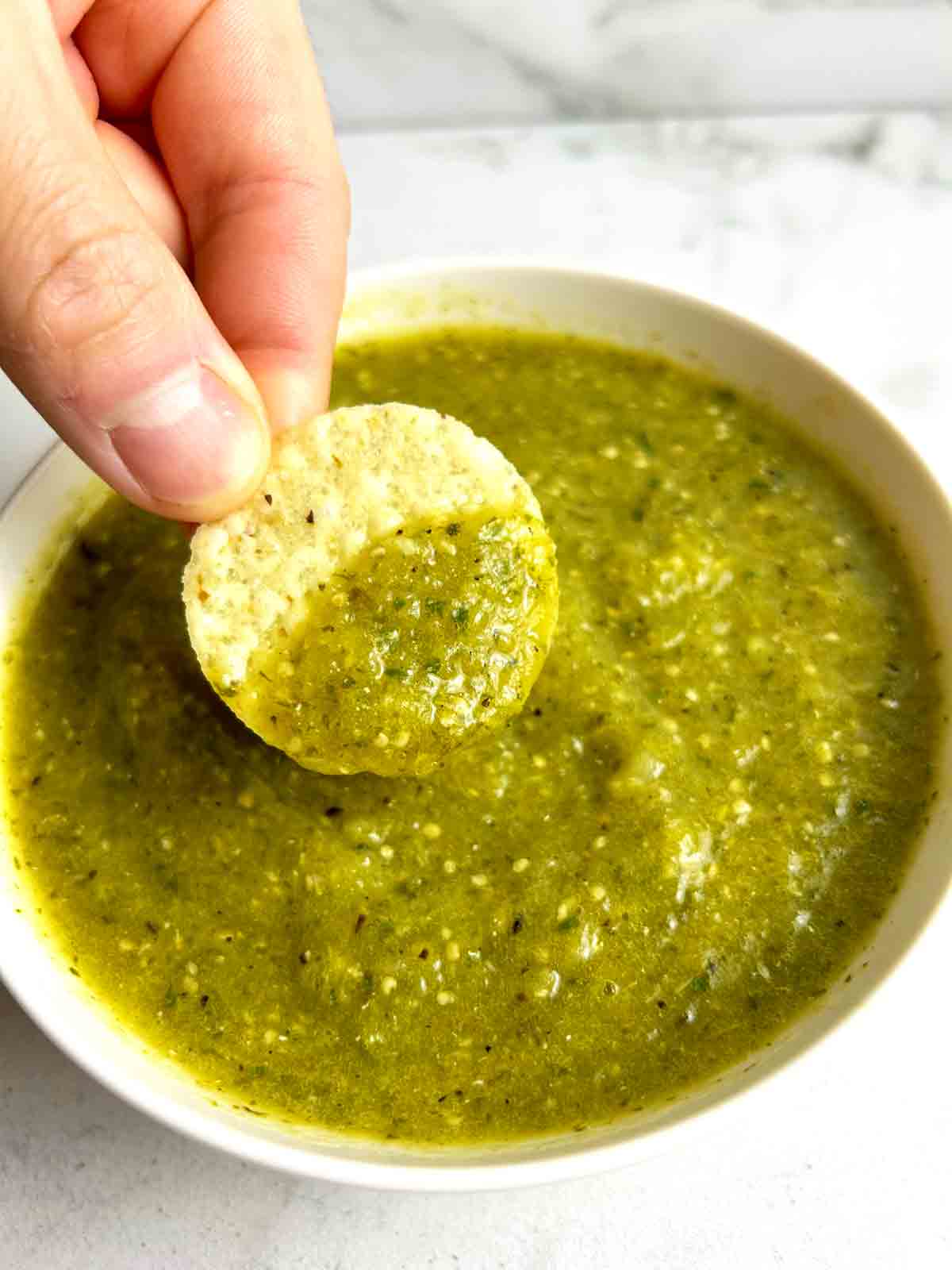 chip being dipped into salsa verde in white bowl.