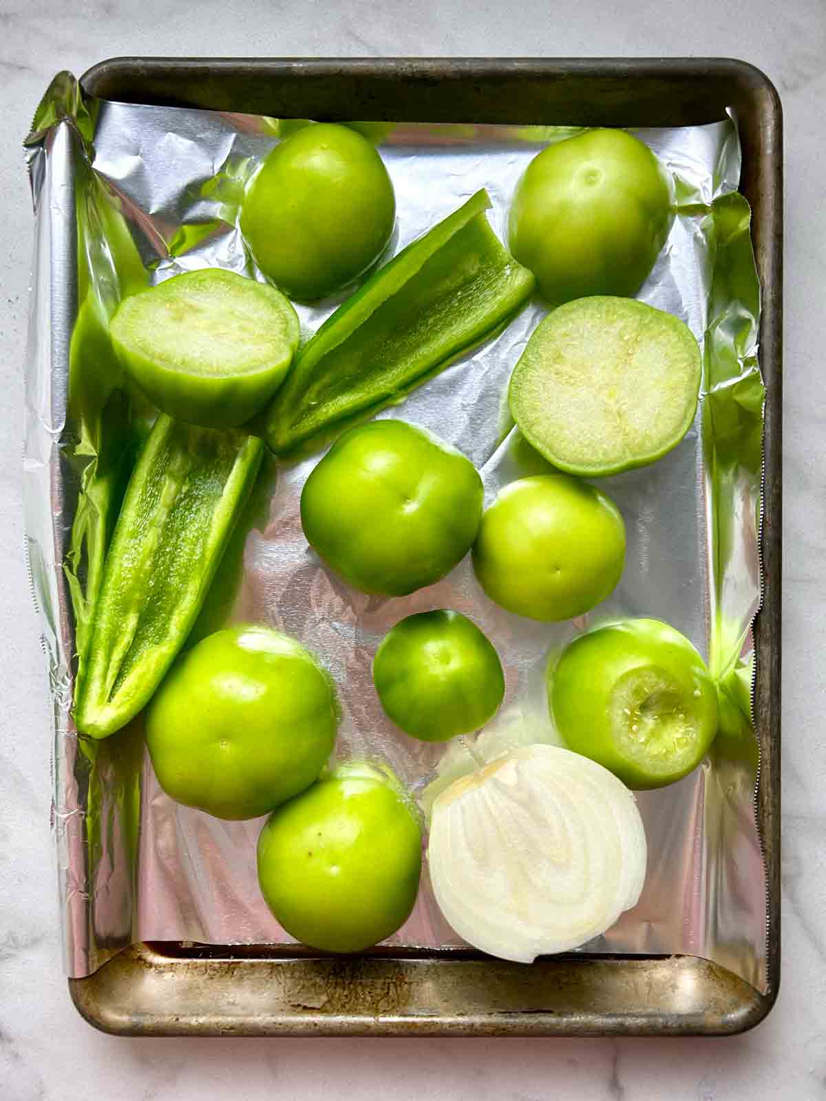 tomatillos, jalapeรฑos, and half an onion on baking sheet.