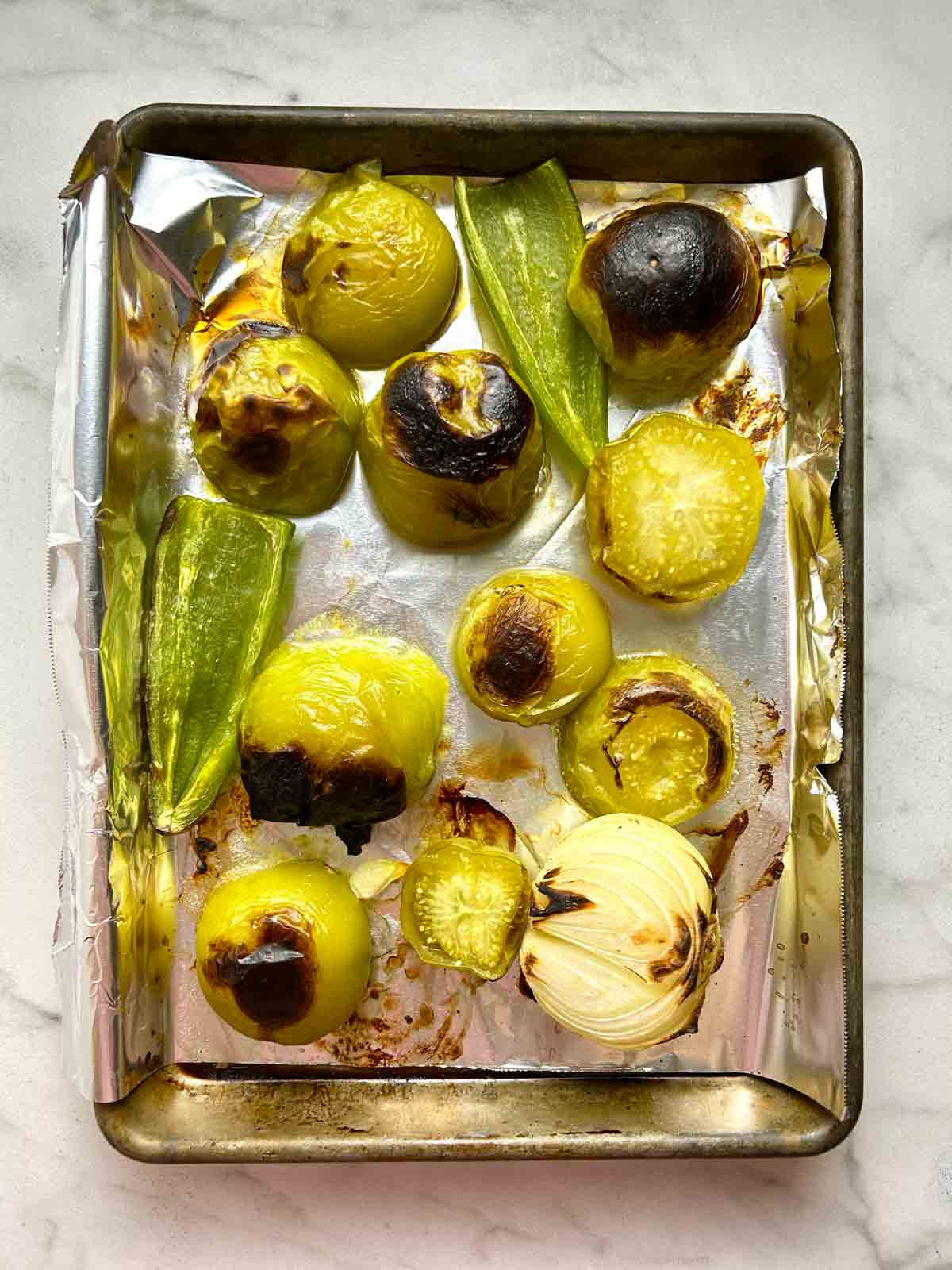 tomatillos, jalapeรฑos, and half an onion after roasting; visibly charred.