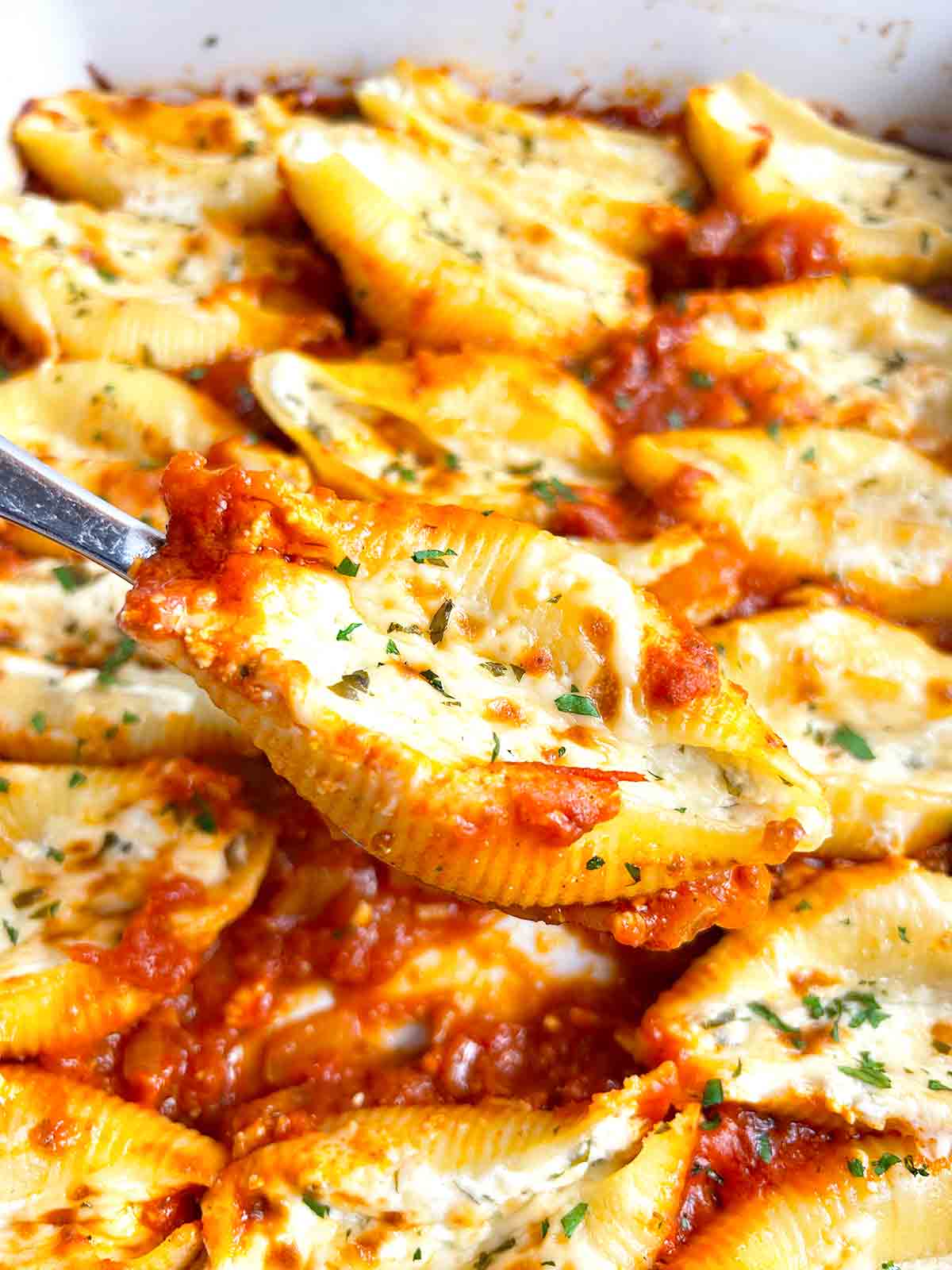 spoon lifting stuffed shell from baking dish.
