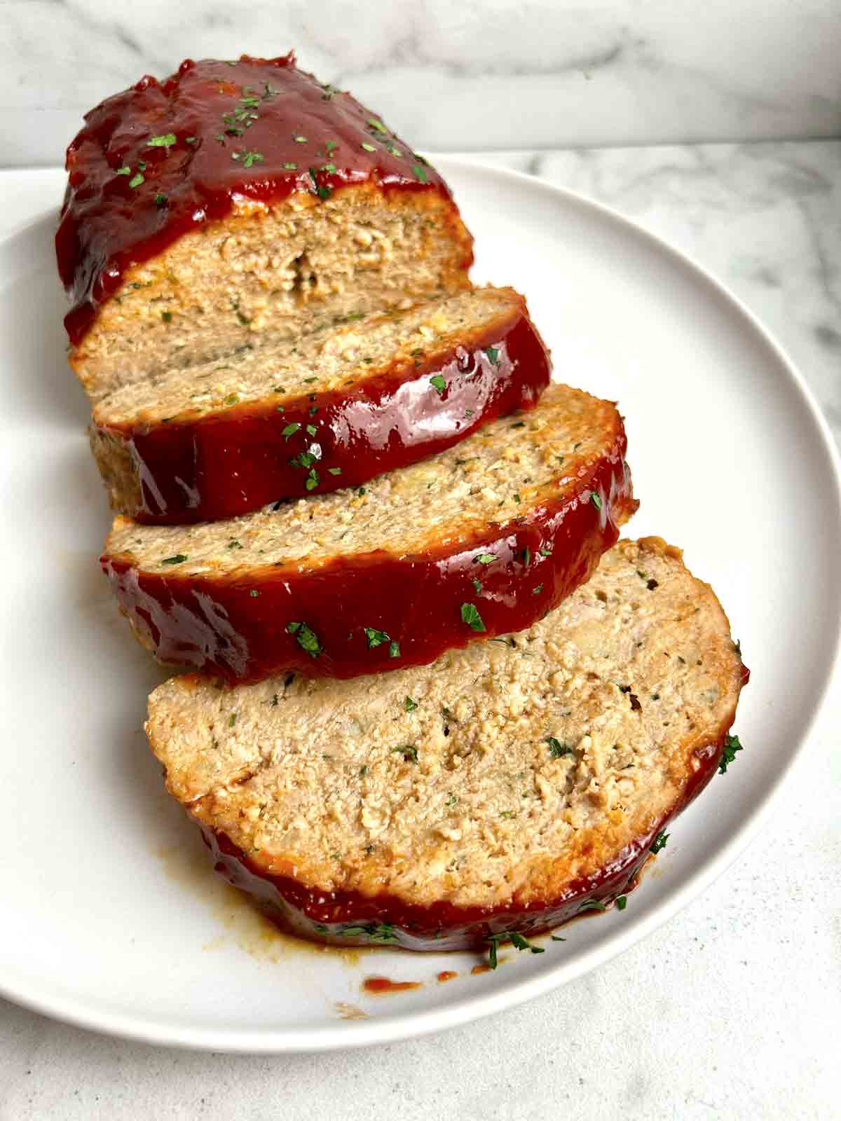 close up of meatloaf sliced into thick pieces on plate.