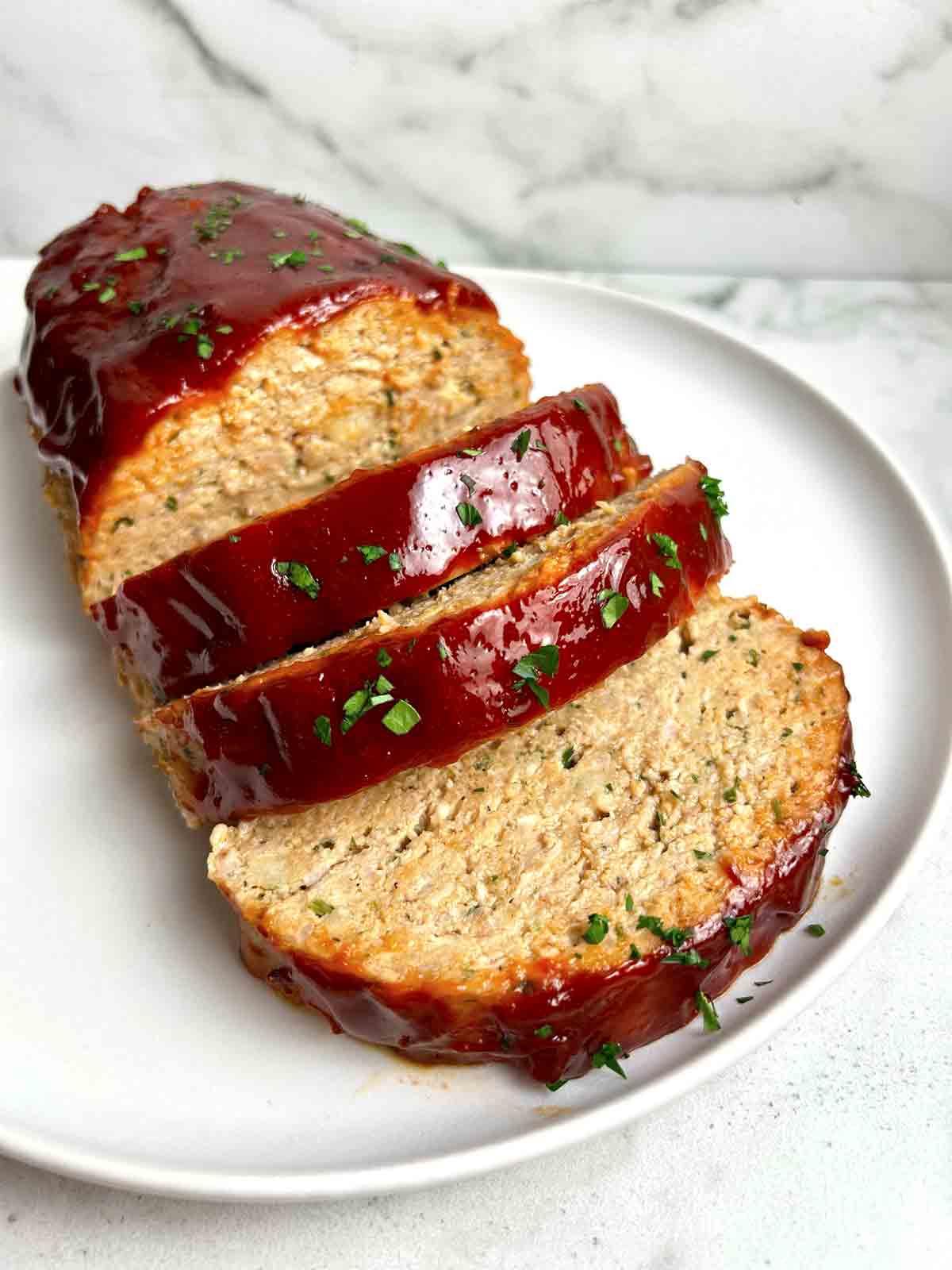 close up of meatloaf sliced into thick pieces on plate.