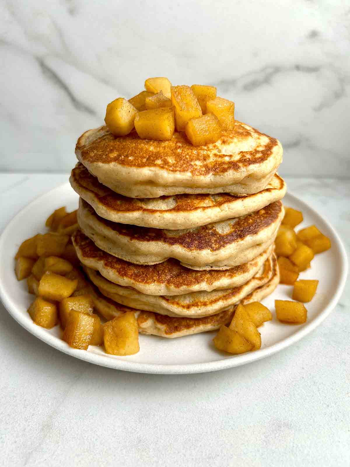 syrup of apple pancakes with diced apples around plate.