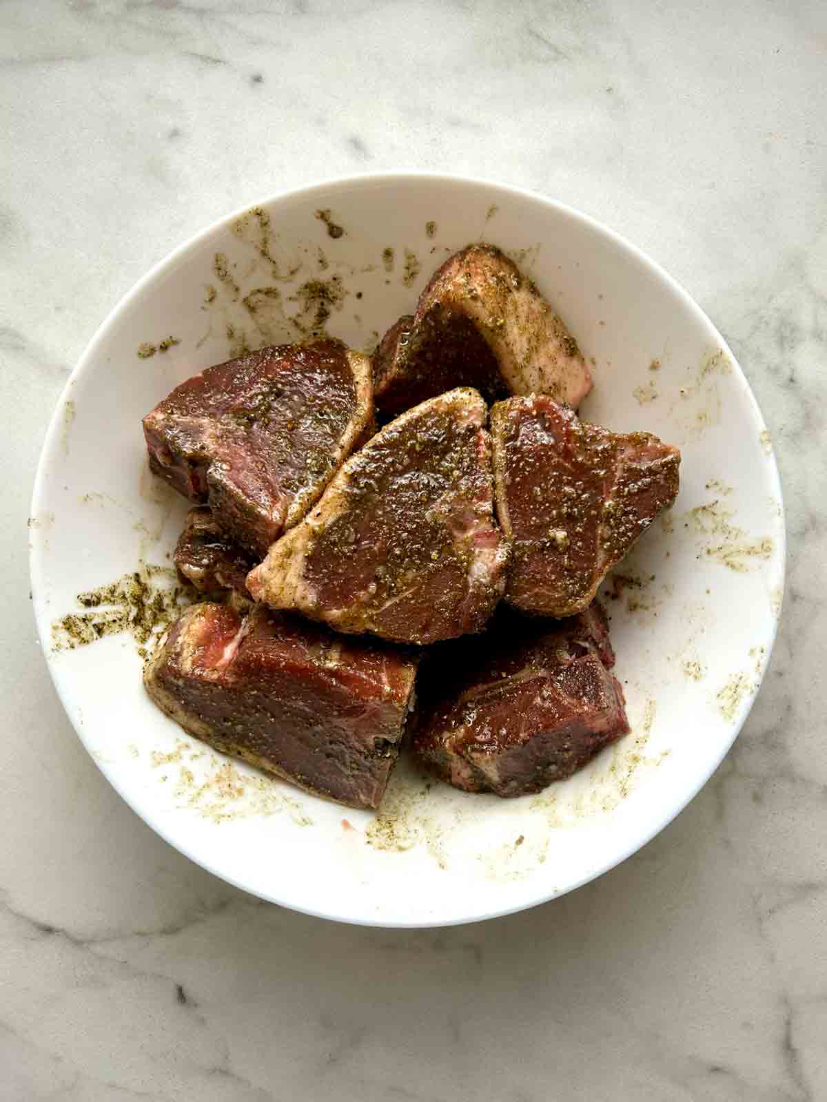 lamb loin chops mixed with oil and seasonings in bowl.
