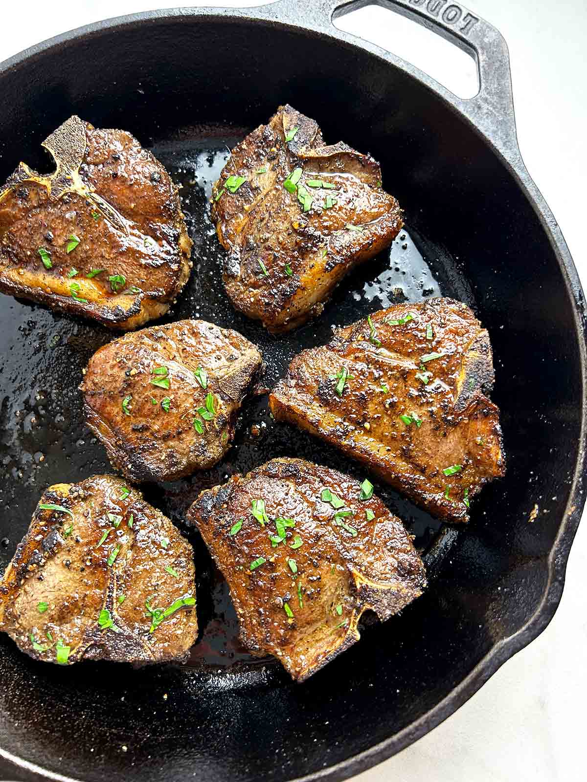 baked lamb loin chops in cast-iron pan with parsley sprinkled on top.