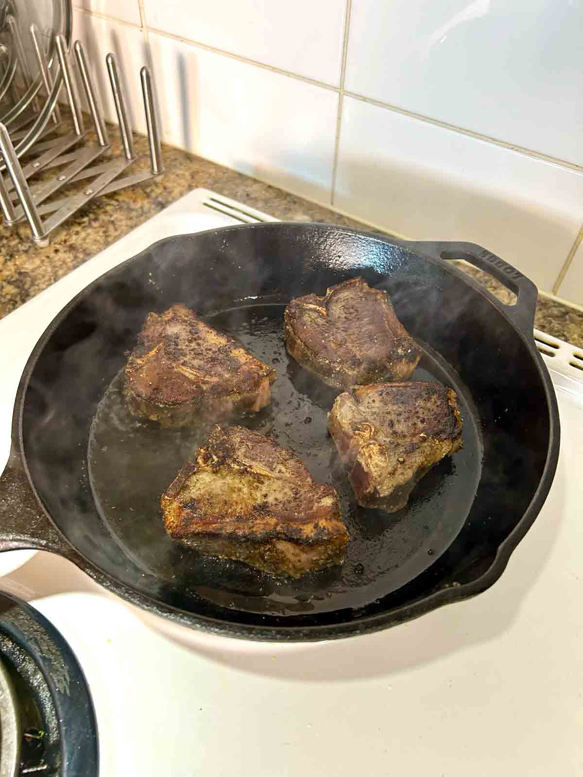 baked lamb loin chops being seared in cast-iron pan.