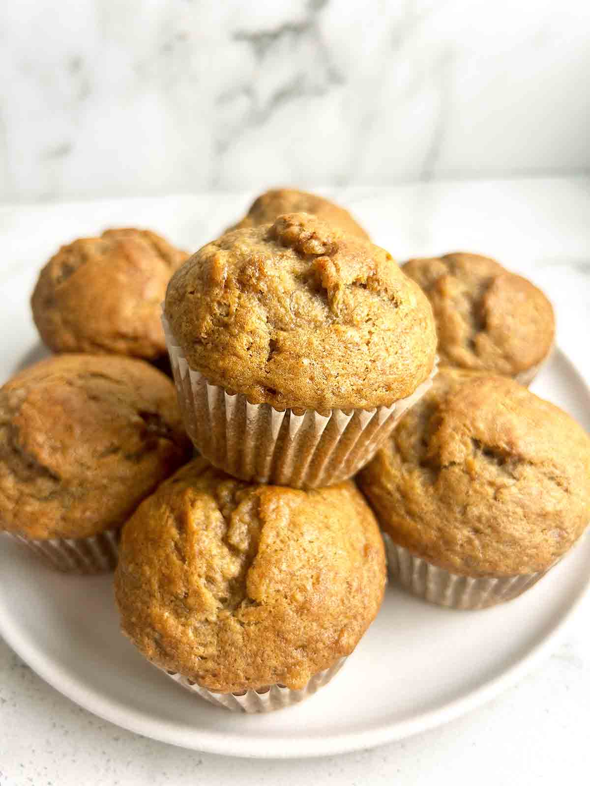 close up of banana muffin on top of other muffins on plate.