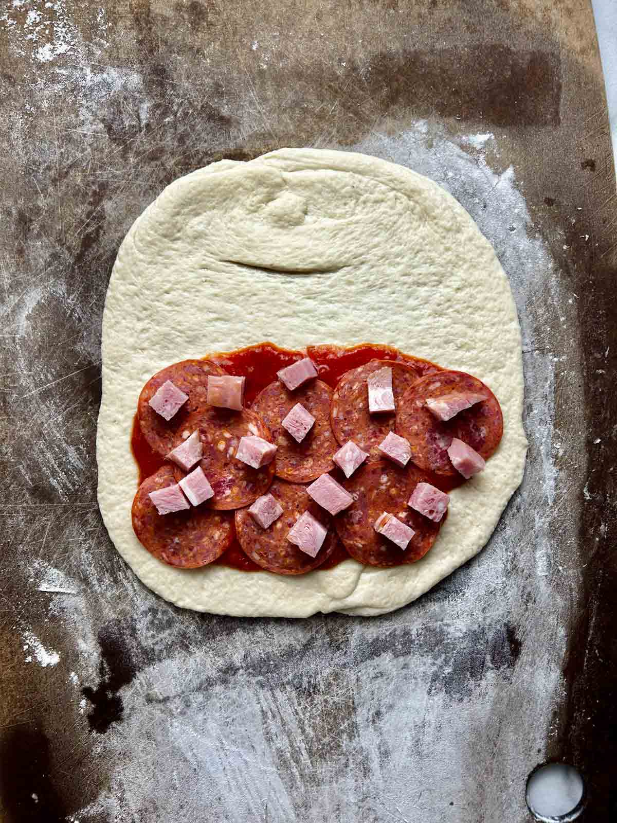 pepperoni and ham added on top of pizza sauce.