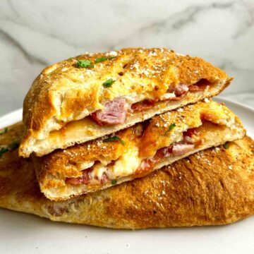 close up of calzone cut in half to show melting cheese and toppings.