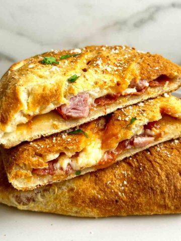 close up of calzone cut in half to show melting cheese and toppings.
