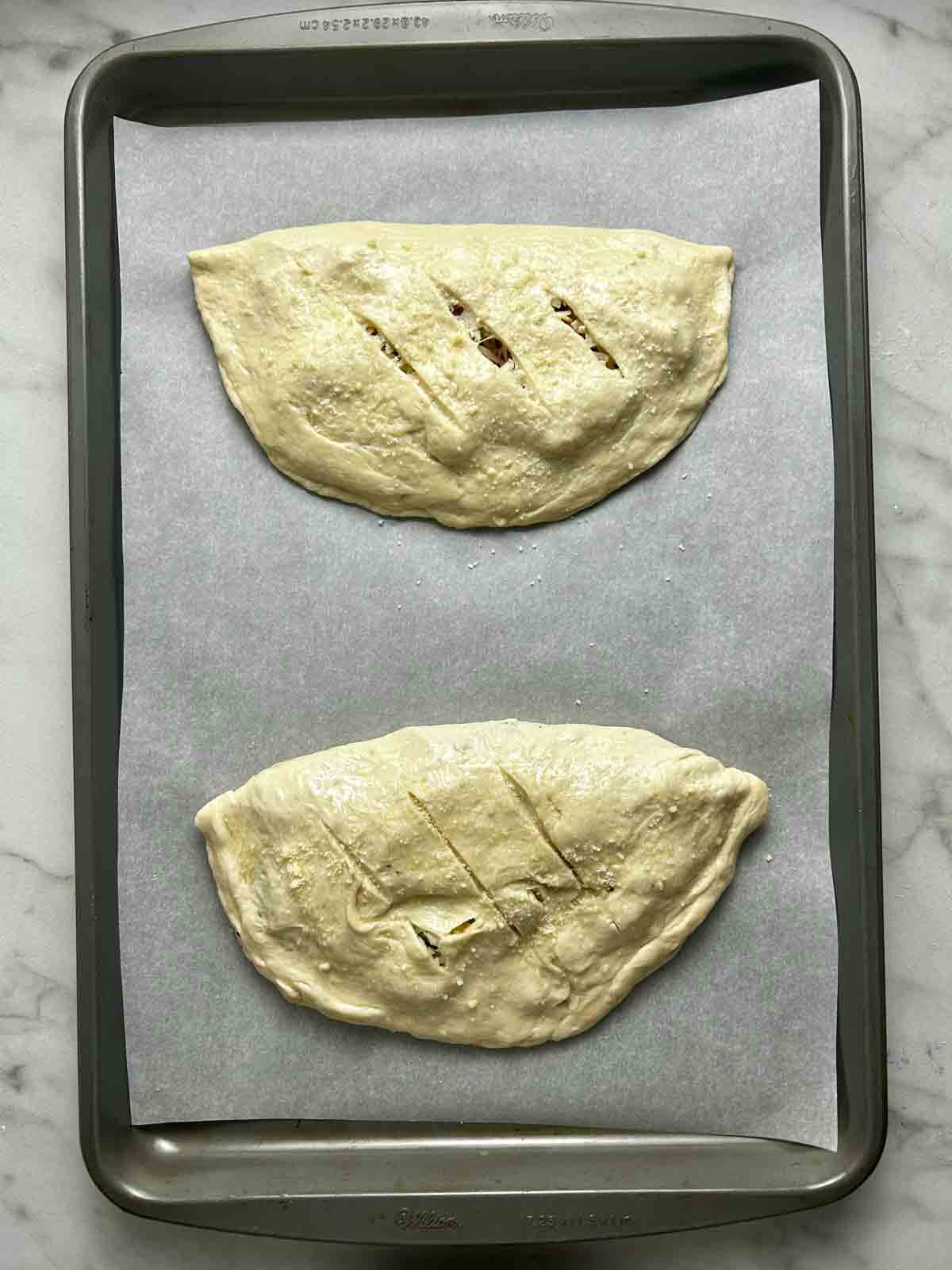 calzones on baking sheet with slits cut on top.