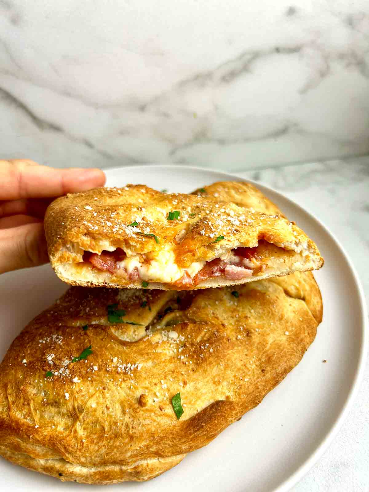 hand lifting half of calzone off plate.