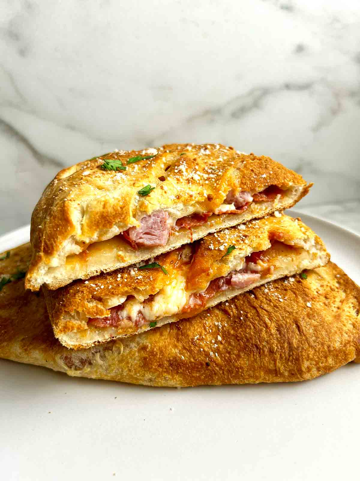close up of calzone cut in half to show melting cheese and toppings.