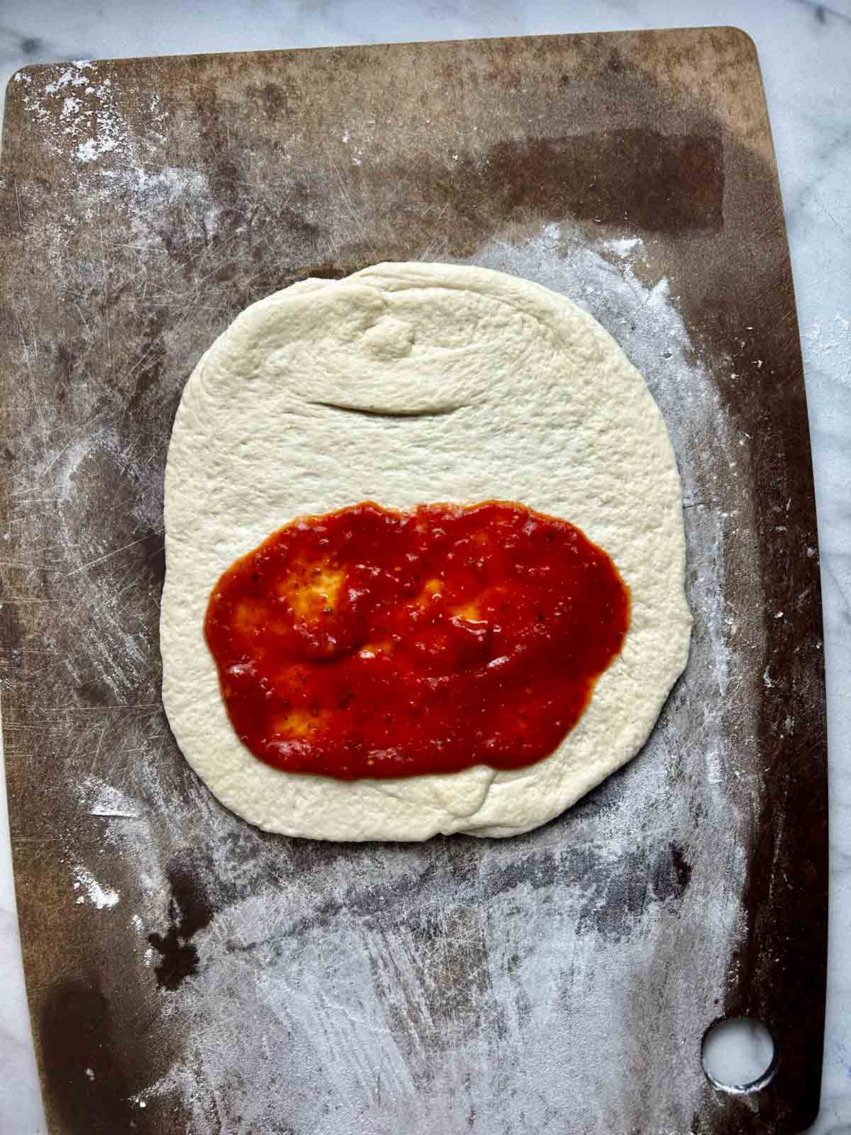 pizza sauce spread on bottom half of dough.