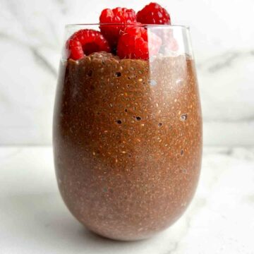 chocolate chia pudding in glass cup with fresh raspberries on top.