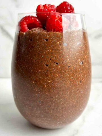 chocolate chia pudding in glass cup with fresh raspberries on top.