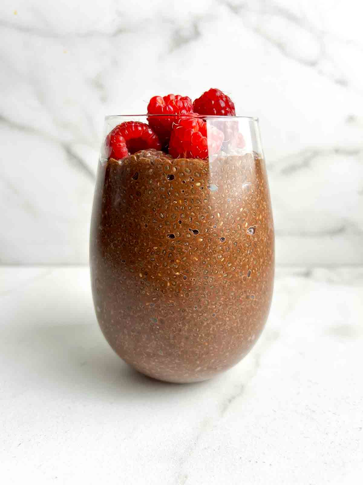 chocolate chia pudding in glass cup with fresh raspberries on top.
