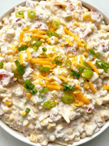 crack corn dip in bowl with extra cheddar cheese and green onions sprinkled on top.