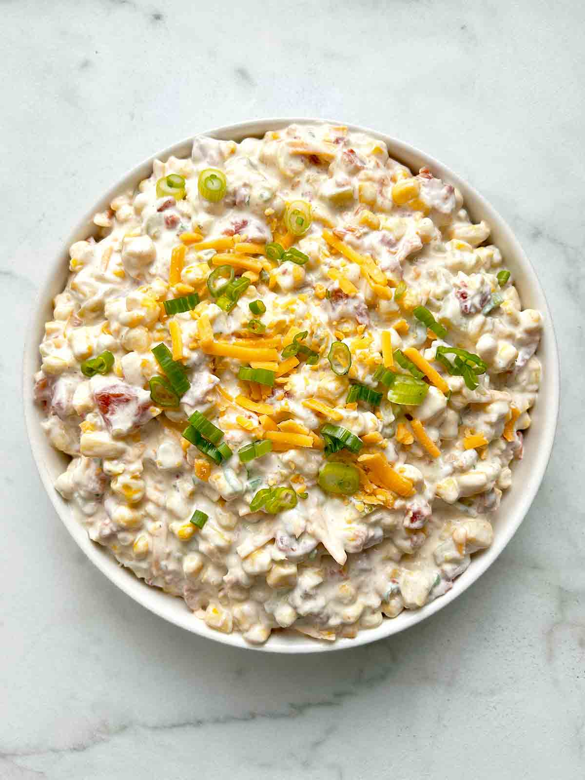 crack corn dip in bowl with extra cheddar cheese and green onions sprinkled on top.