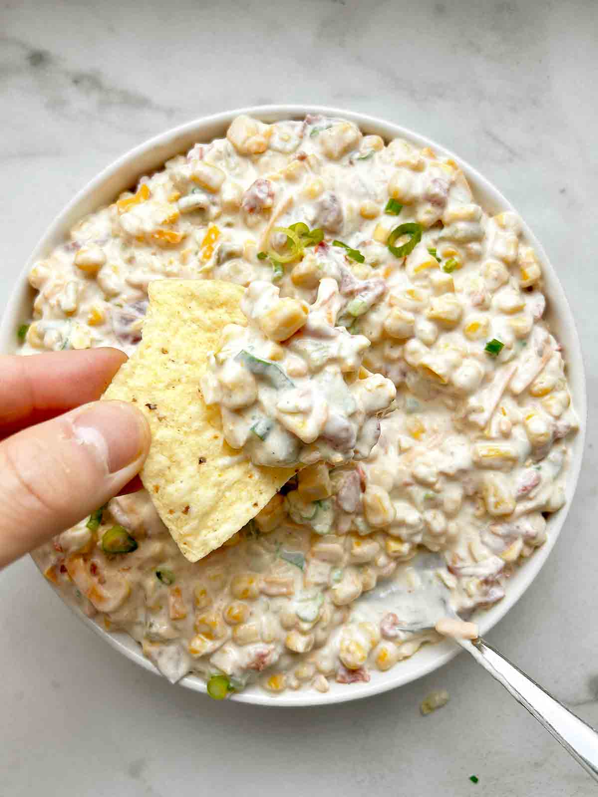 tortilla chip scooping corn dip from bowl.