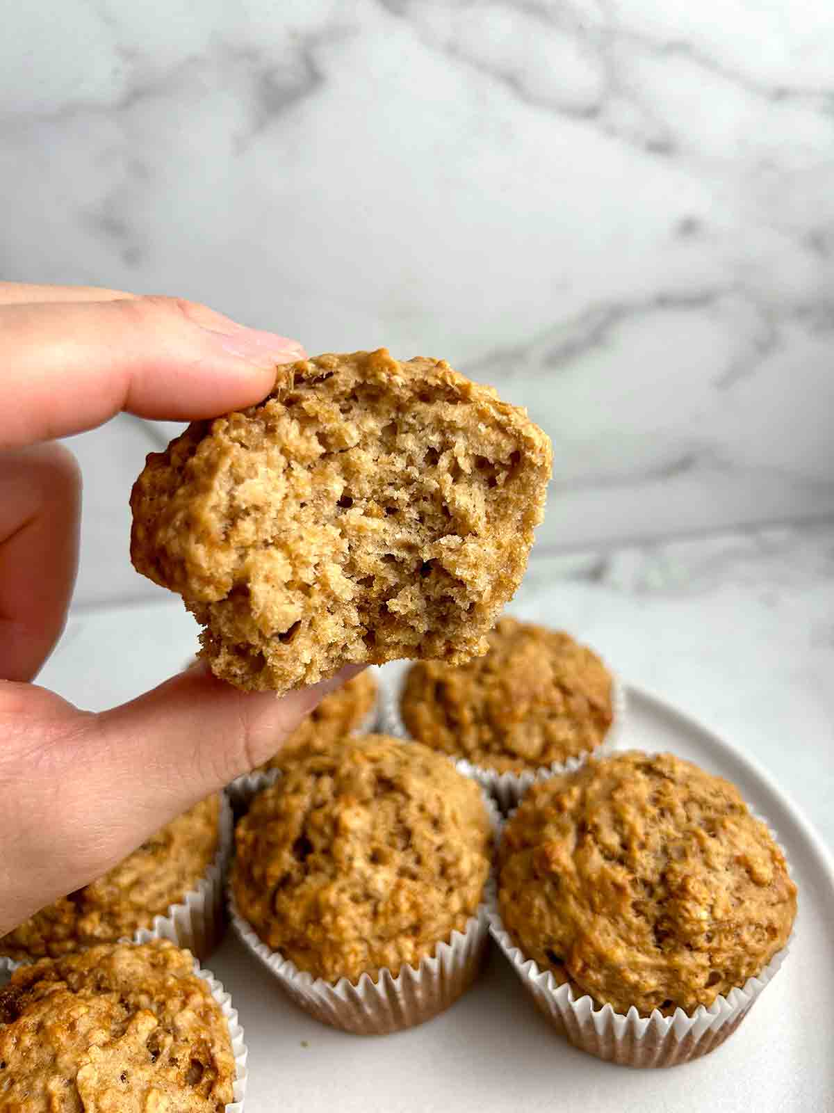 hand pinching oatmeal applesauce muffins with bite taken out of it.