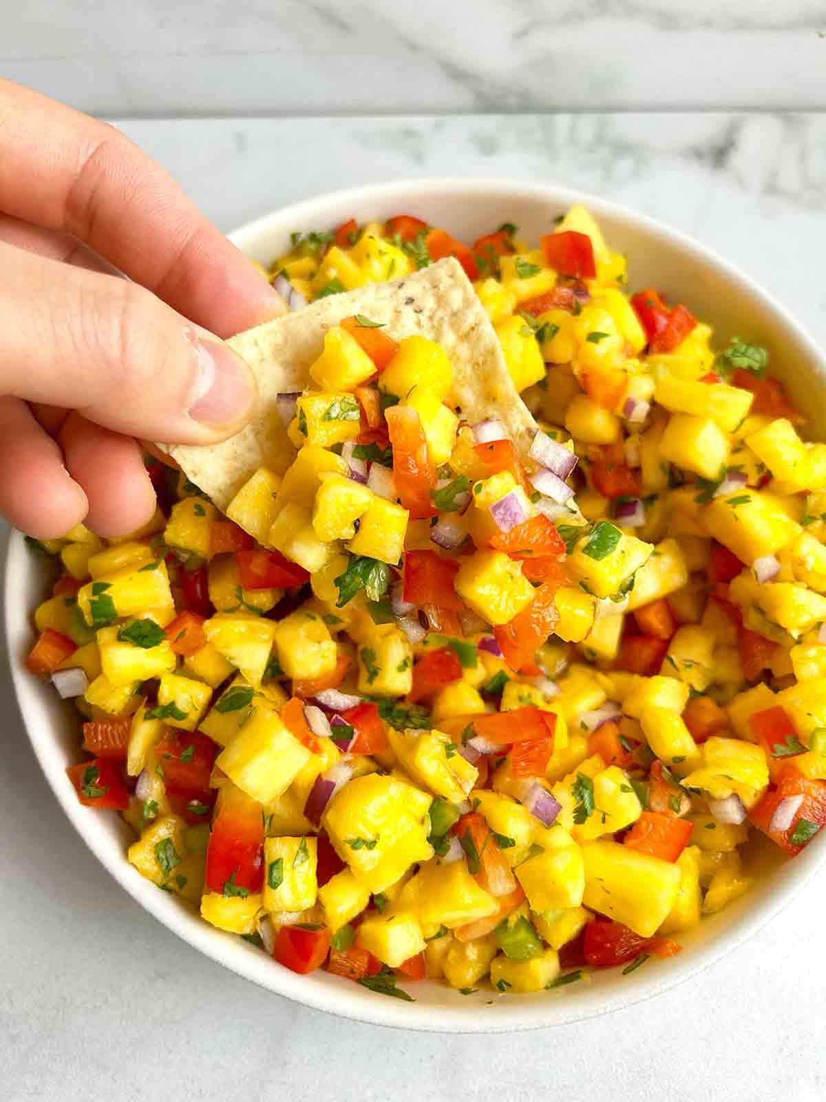 tortilla chip scooping salsa from bowl.