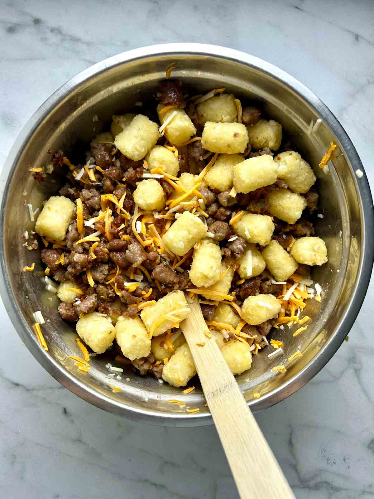 tater tots, breakfast sausages, and cheeses tossed in bowl.
