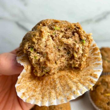 hand holding zucchini banana muffin with bite taken out of it.