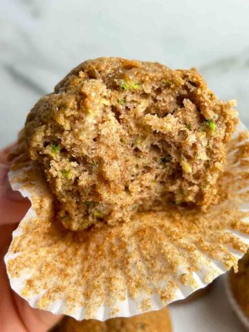hand holding zucchini banana muffin with bite taken out of it.