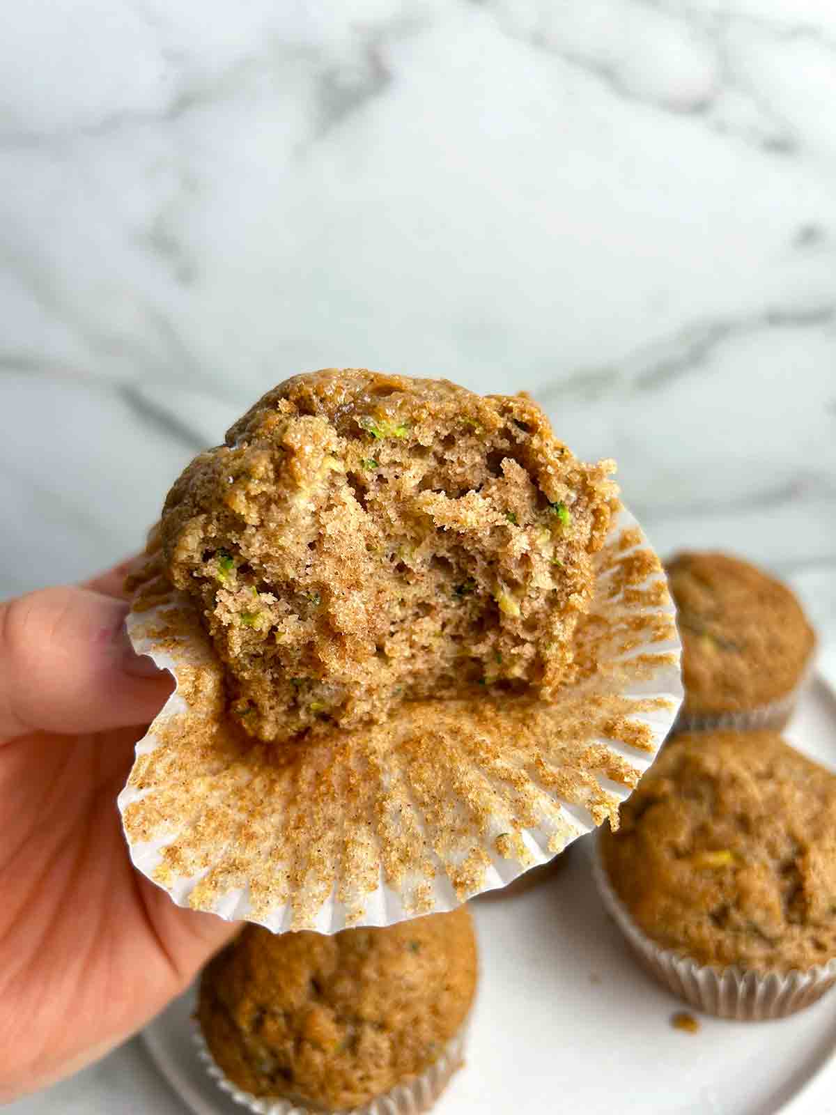 hand holding zucchini banana muffin with bite taken out of it.