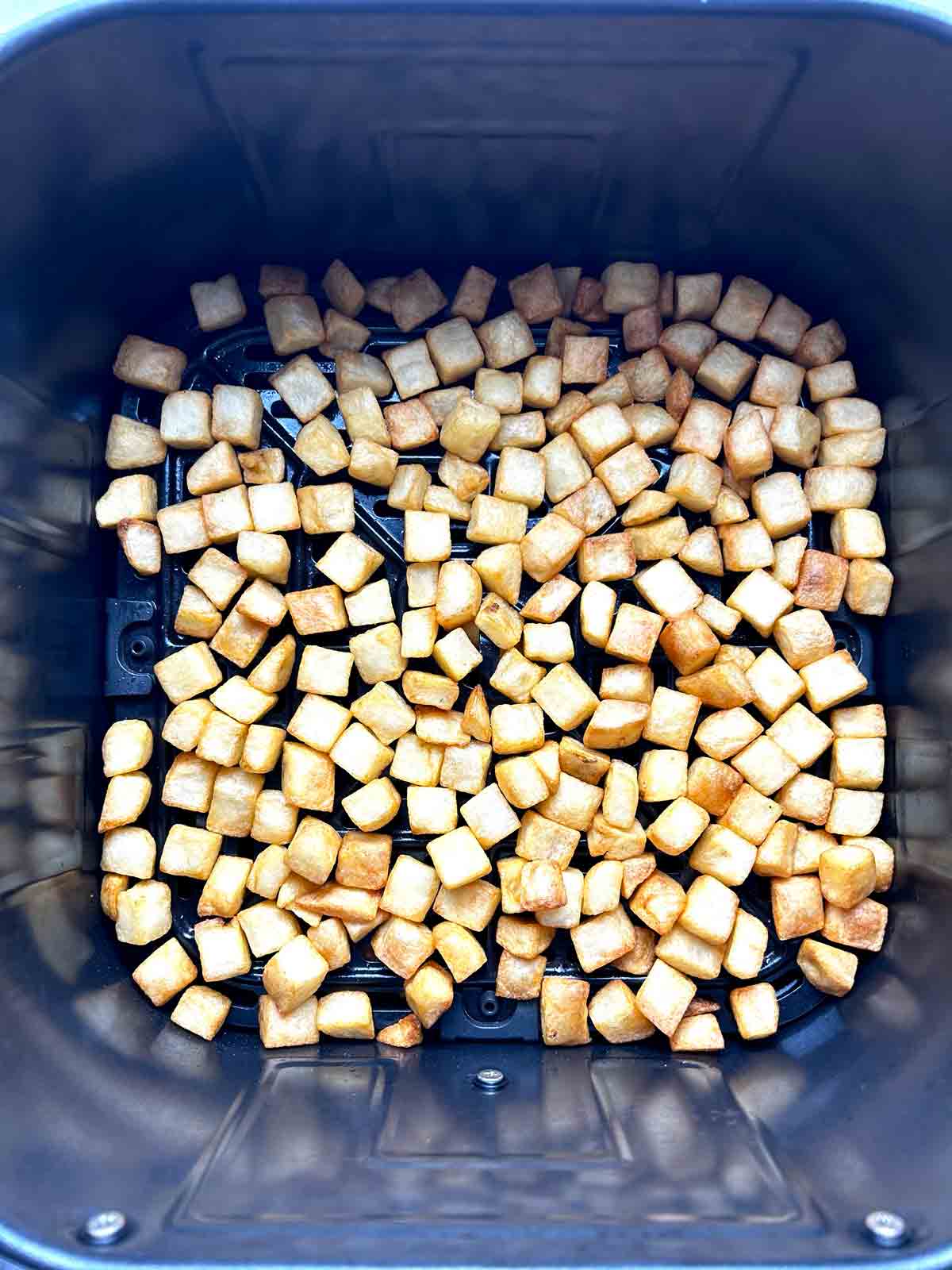 diced hash browns in air fryer basket.
