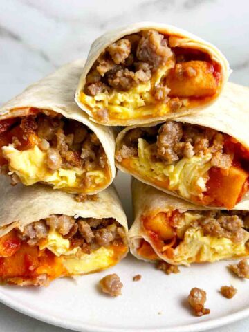 stack of cut-in-half breakfast burritos on white plate.