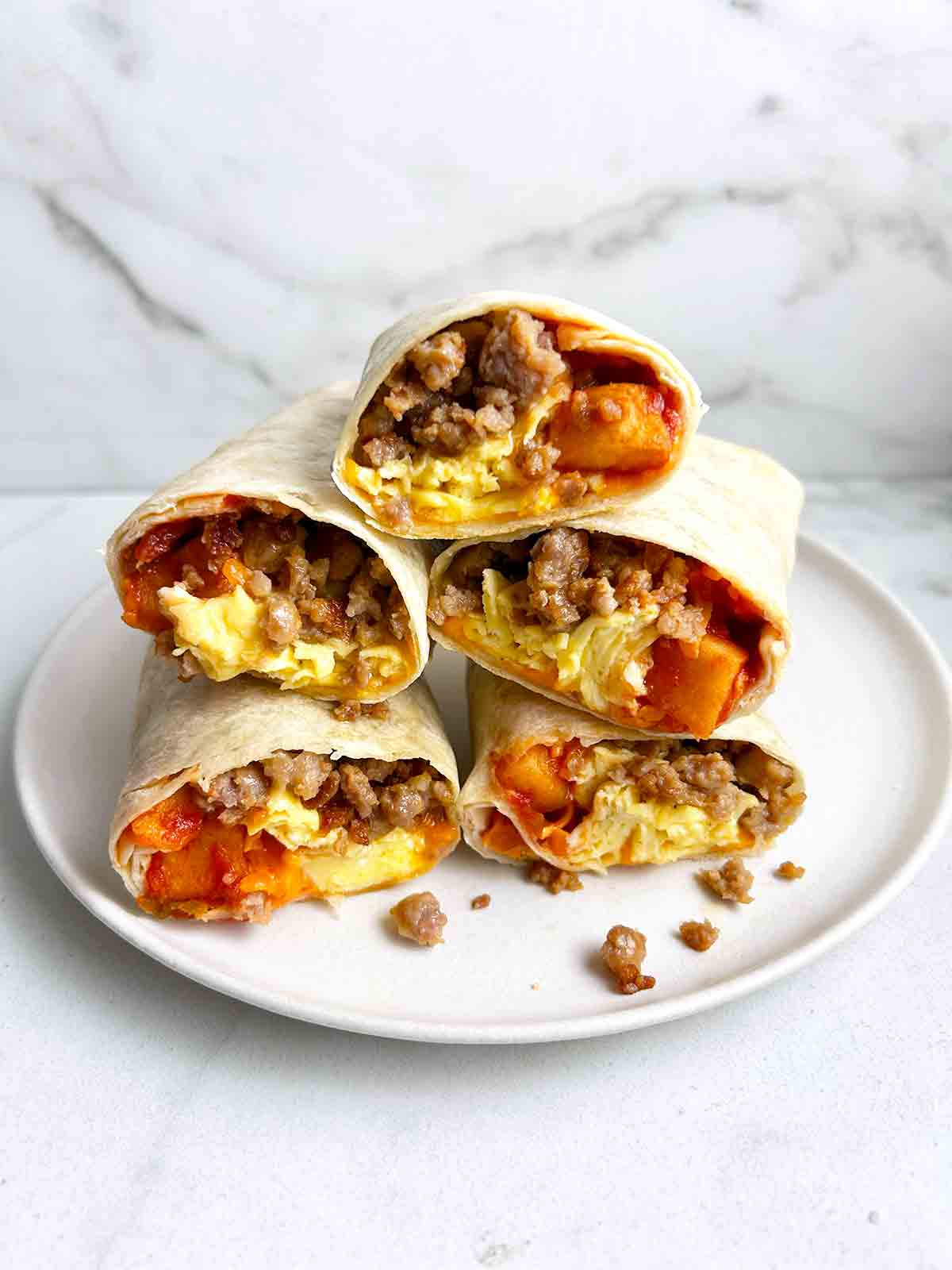 stack of cut-in-half breakfast burritos on white plate.