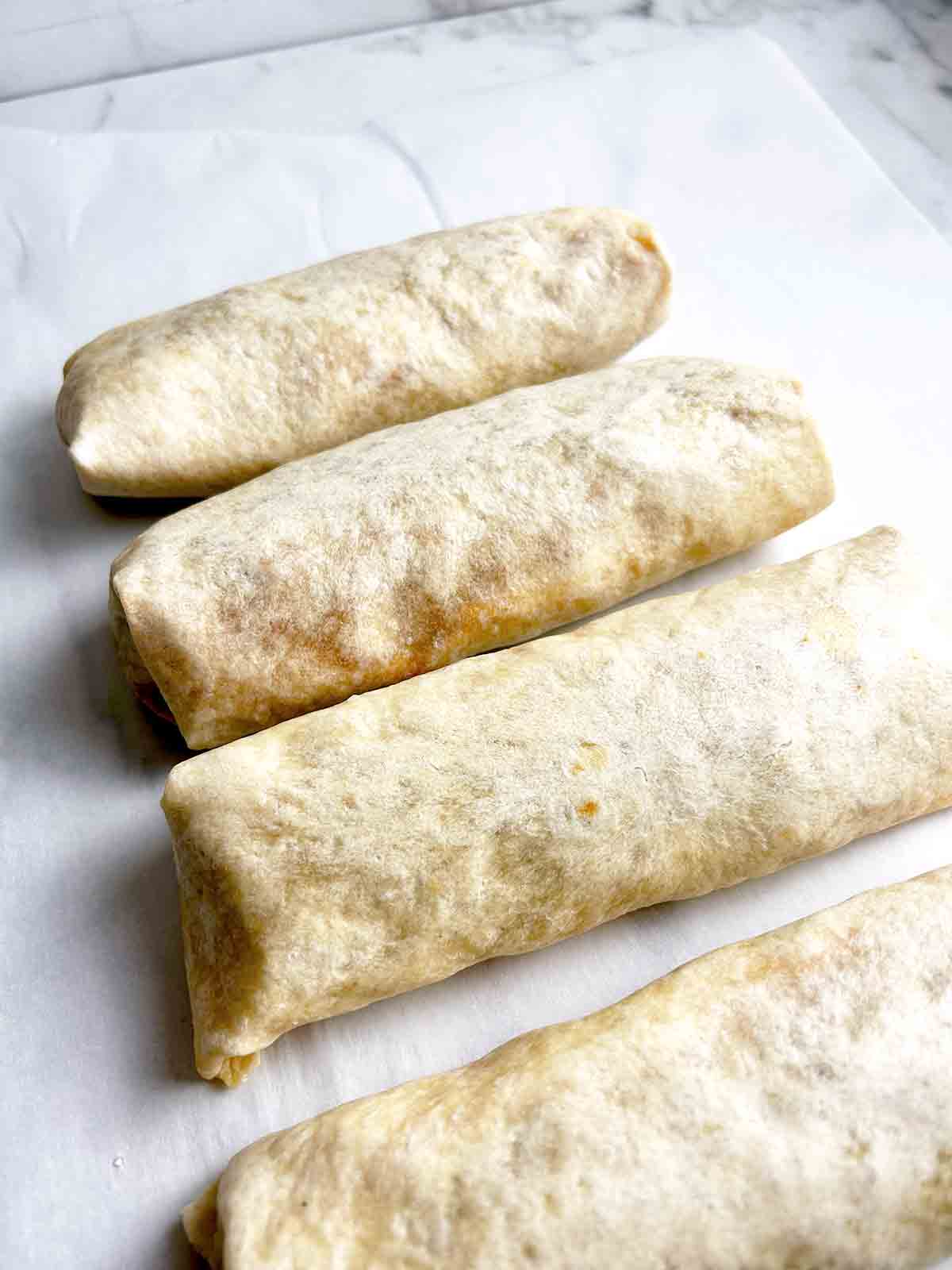 4 breakfast burritos on parchment paper.