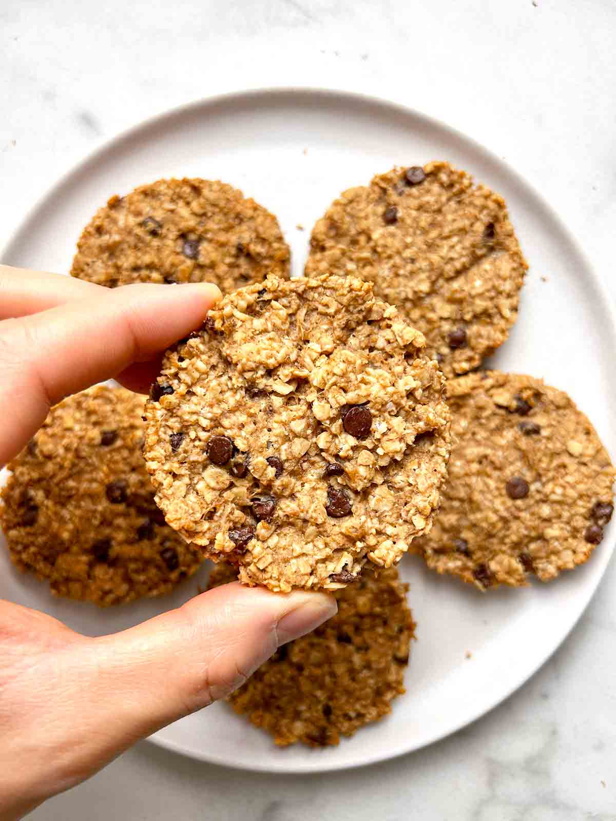 hand holding breakfast cookie over plate of them.